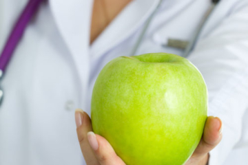 Close up view of medical doctor hand offering green apple